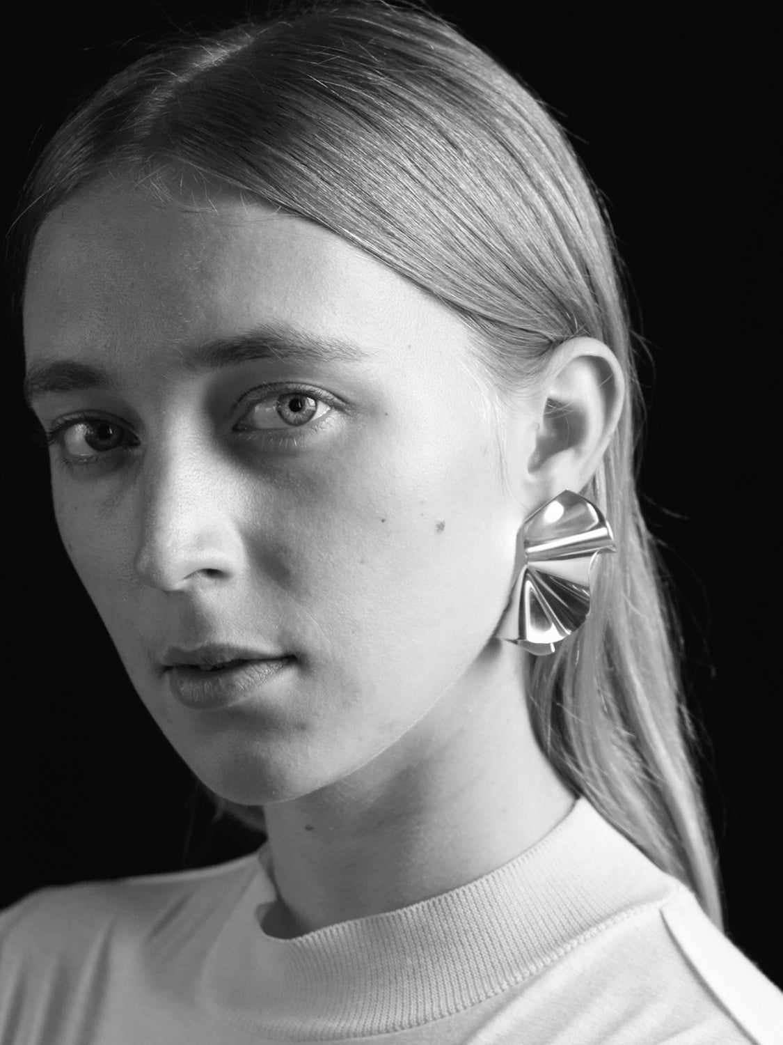 Black and white portrait of a person wearing a unique sculptural silver earring.