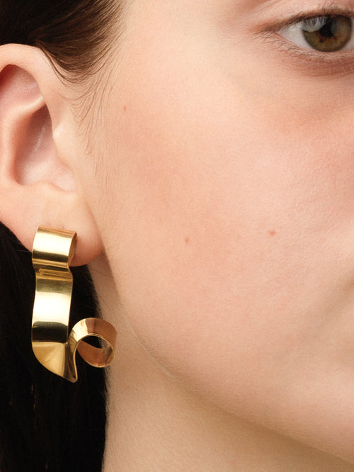 Gold sculptural earring worn by a person