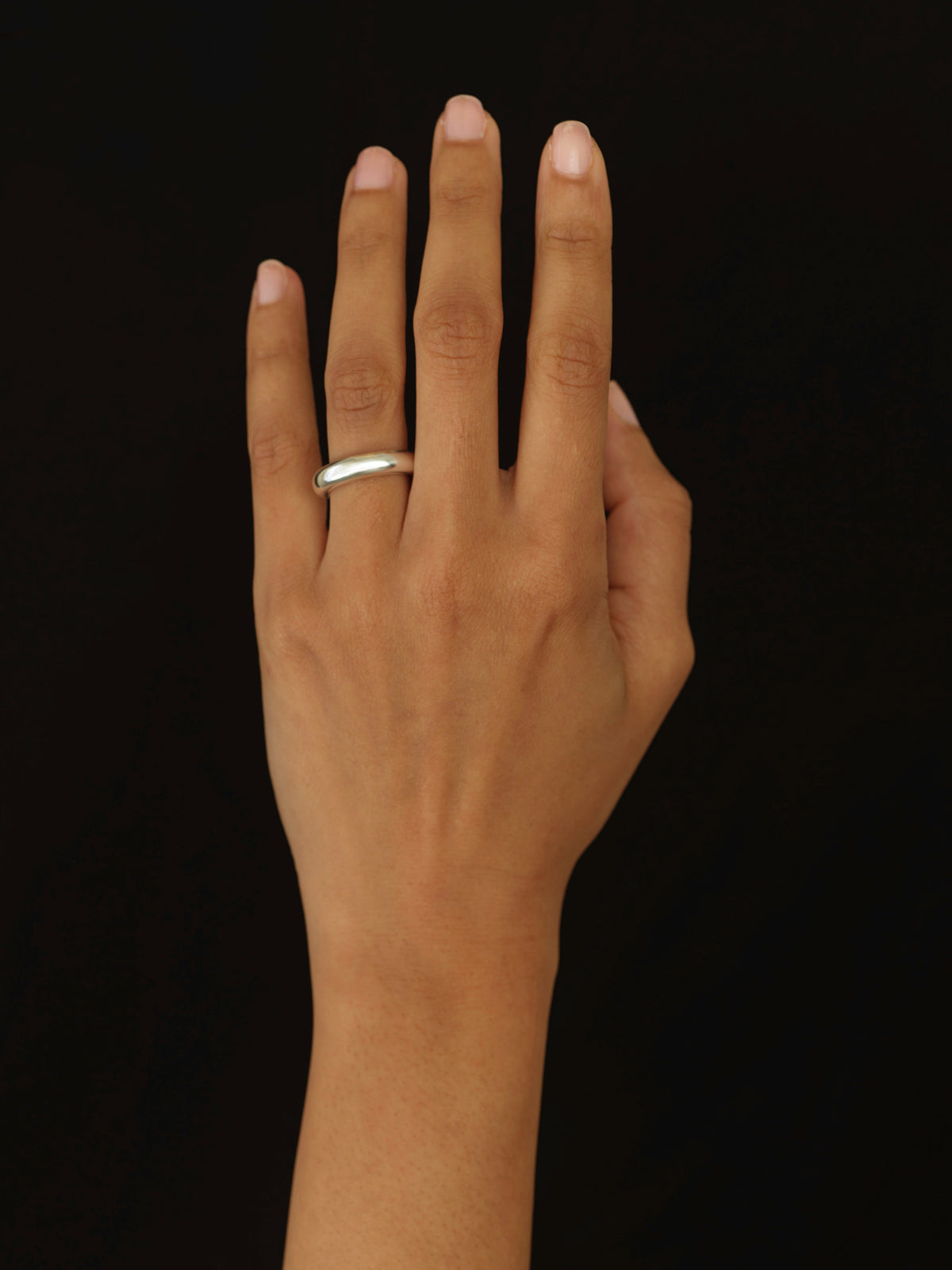 A silver band ring worn on the ring finger of a hand, shown against a solid black background.