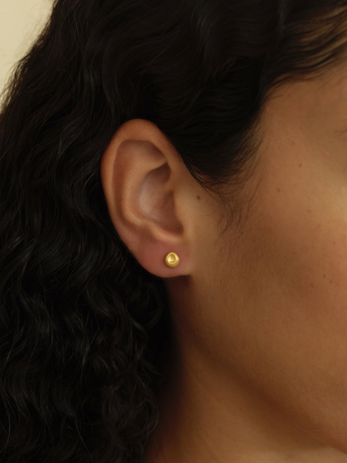 A close-up of a person's ear wearing a small, round gold stud earring.