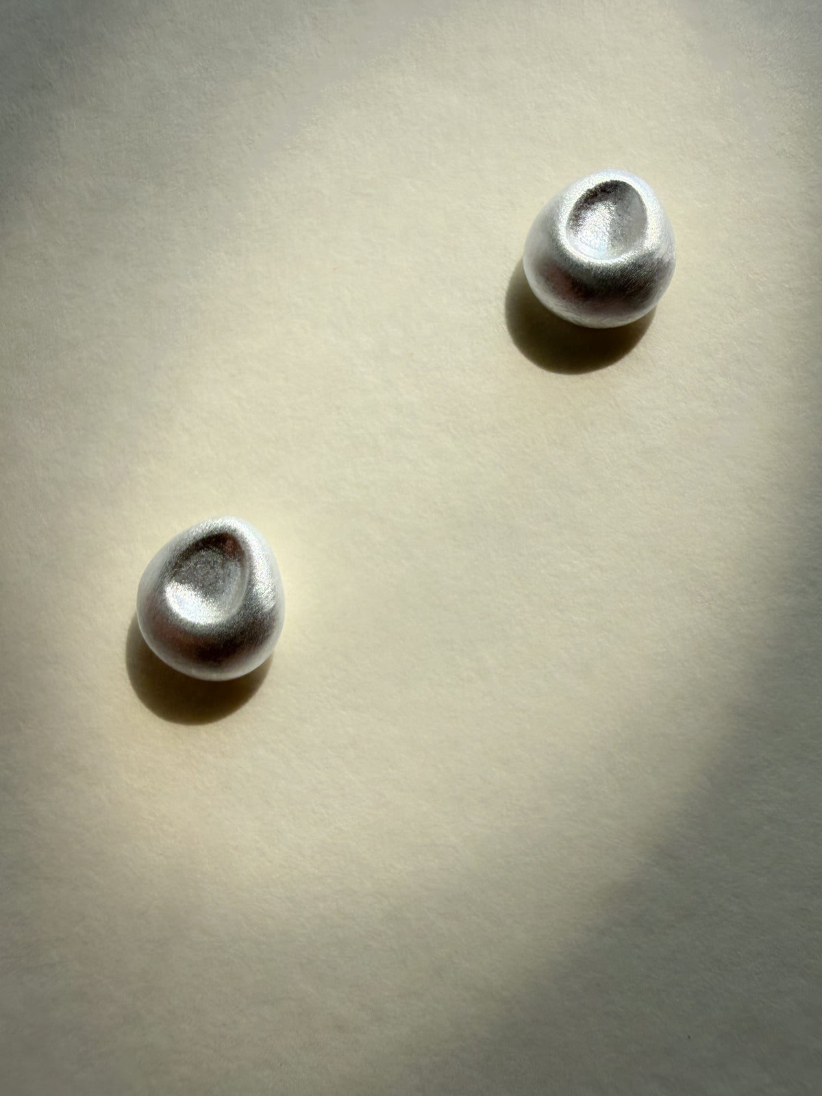 Earring pebble studs in satin brushed silver by Sara Robertsson Jewellery on a beige background.