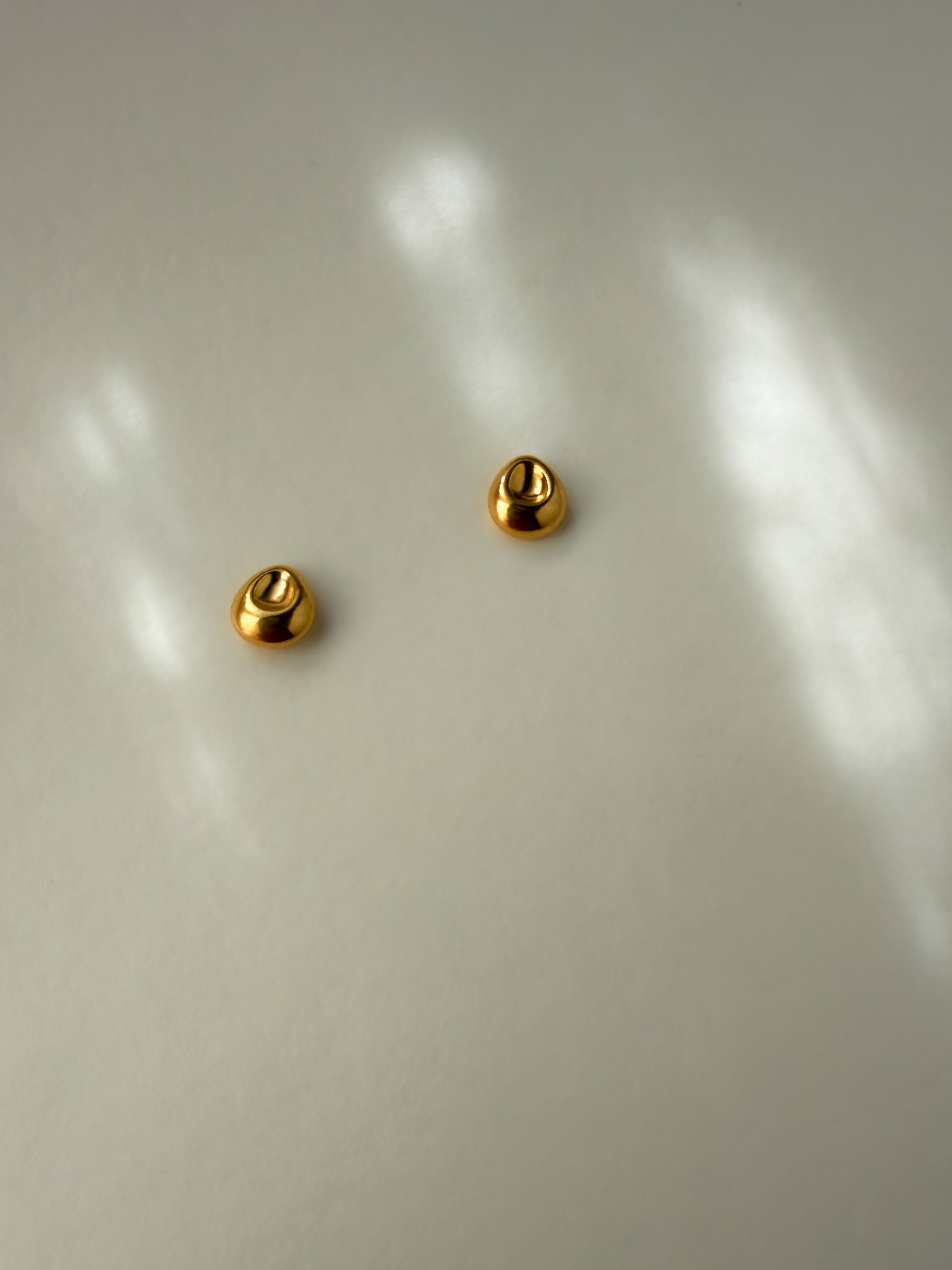 Pebble Stud Earrings in recycled gold vermeil shown from above on a light surface with soft reflections.