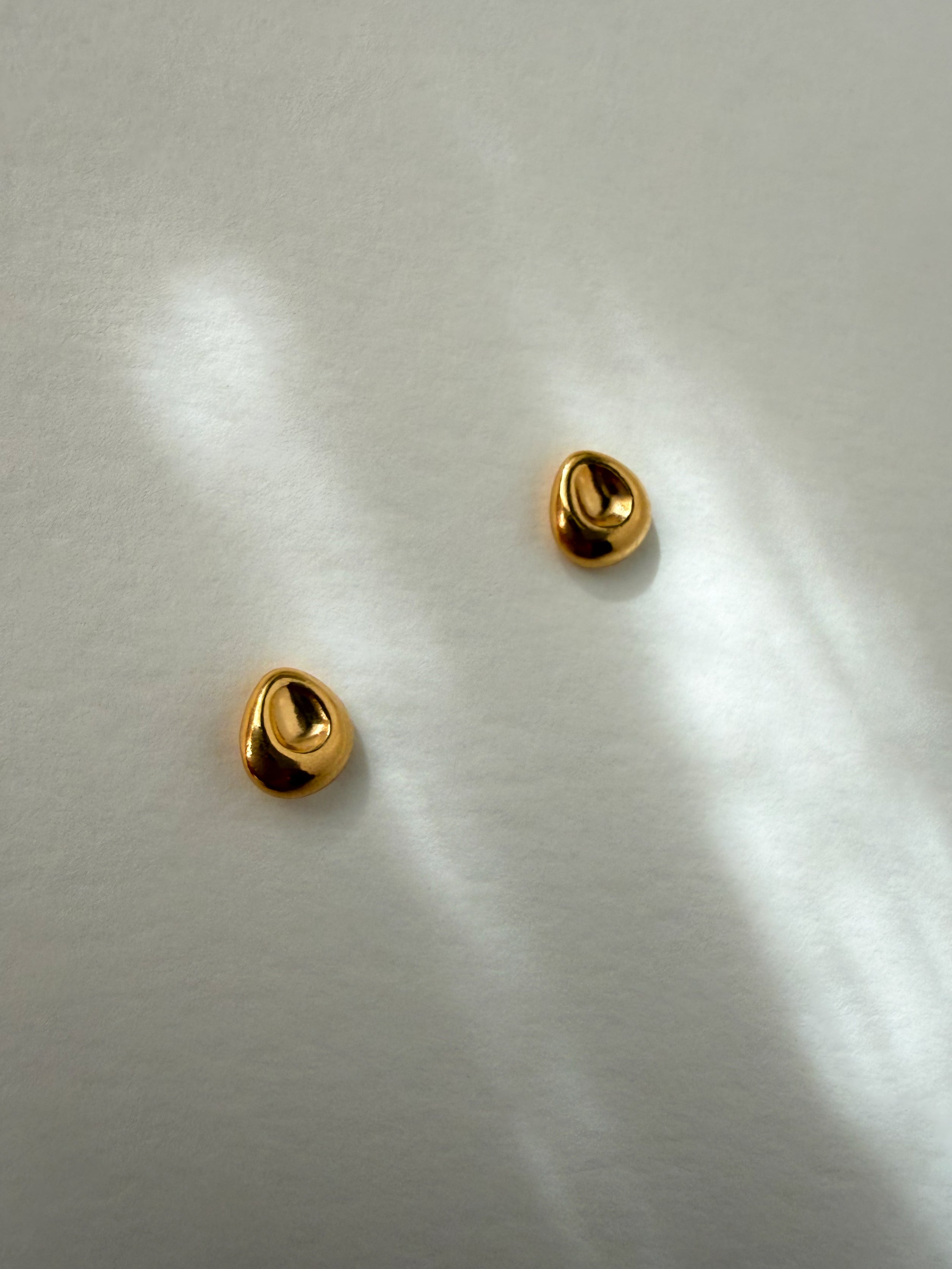 Pebble Stud Earrings in recycled gold vermeil resting on a softly textured surface with reflected light.