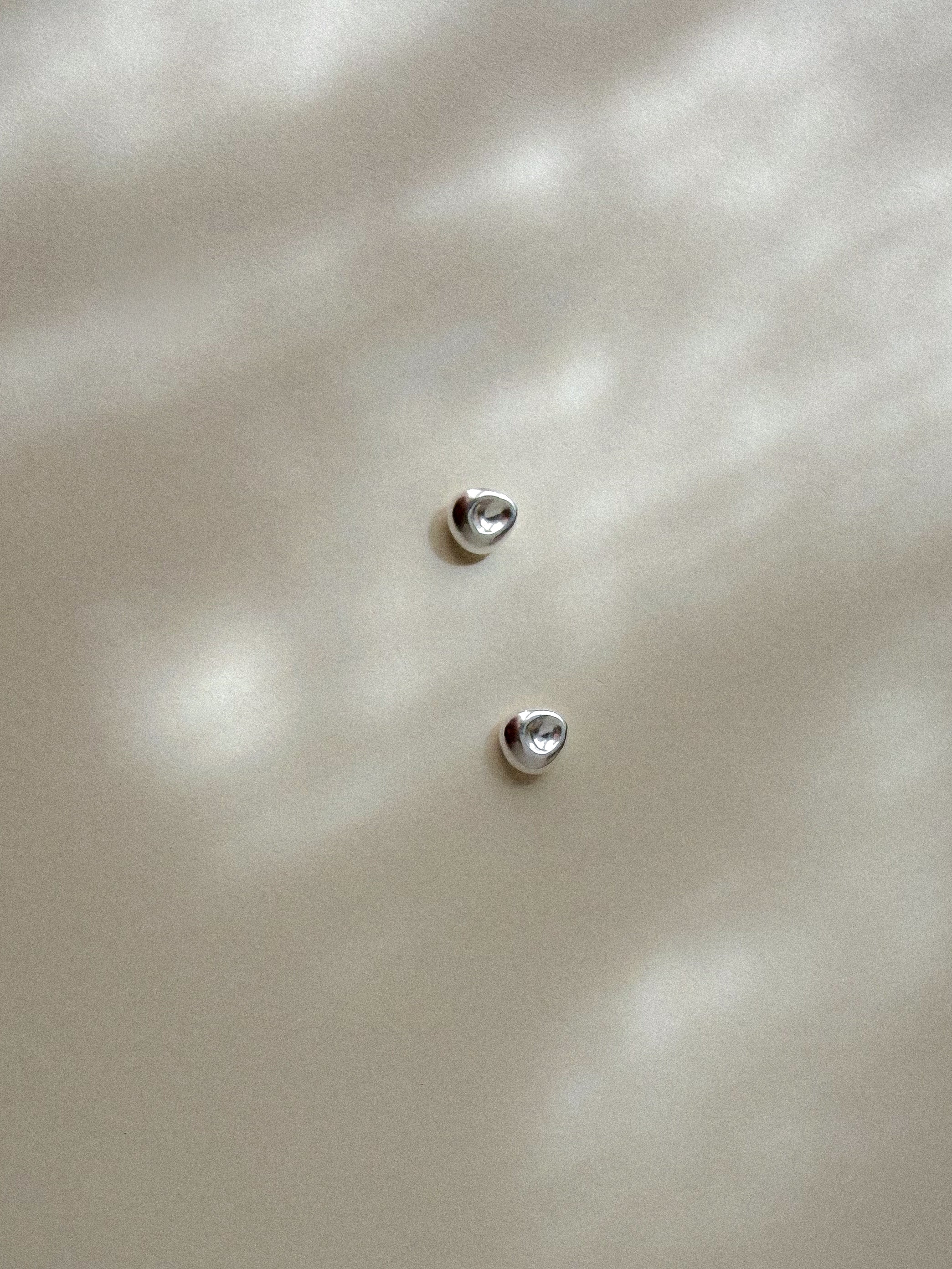 Pebble Stud Earrings in recycled sterling silver on paper in soft natural light.