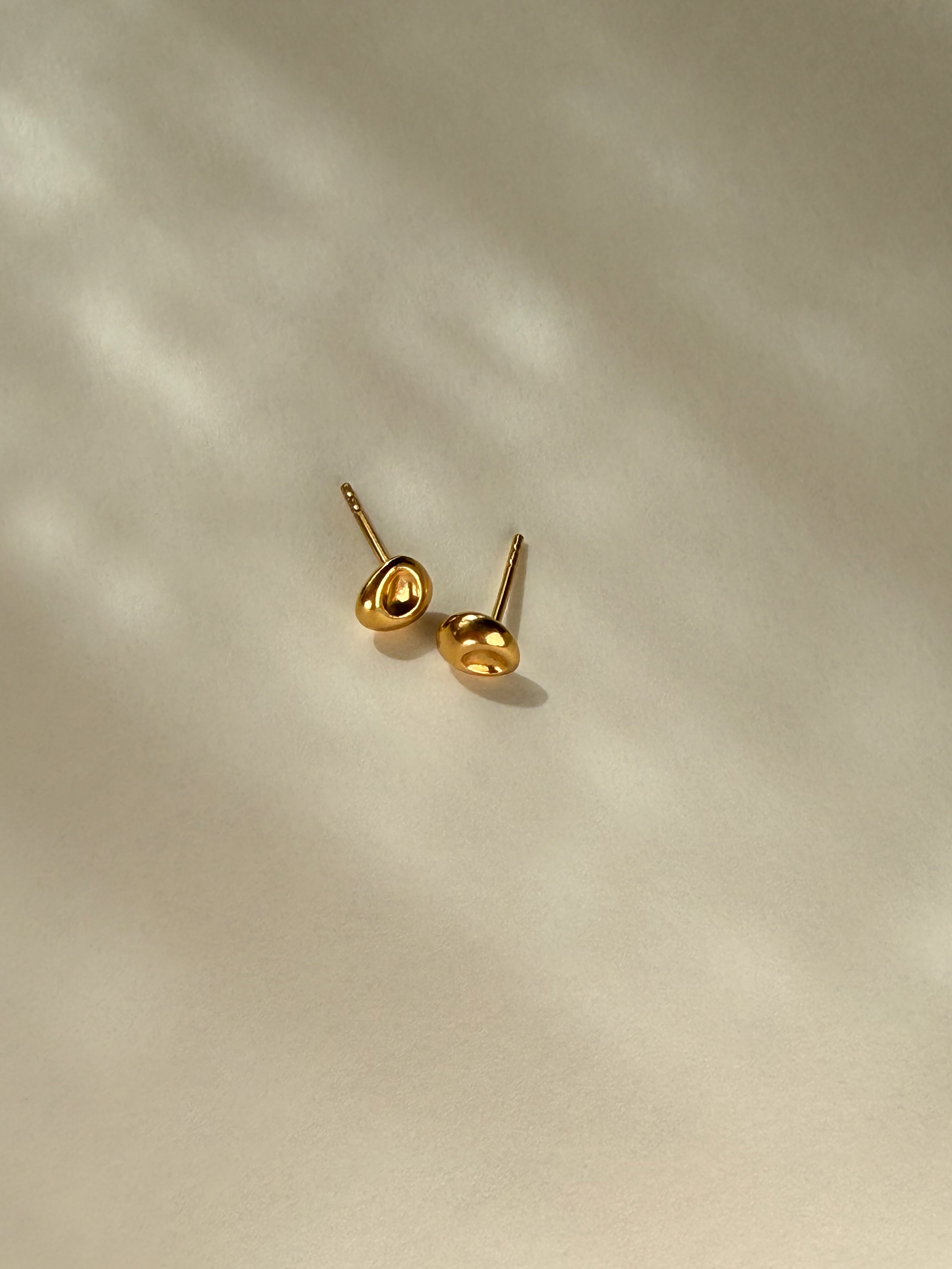 Pebble Stud Earrings in recycled gold vermeil side view on a beige surface with reflected light.