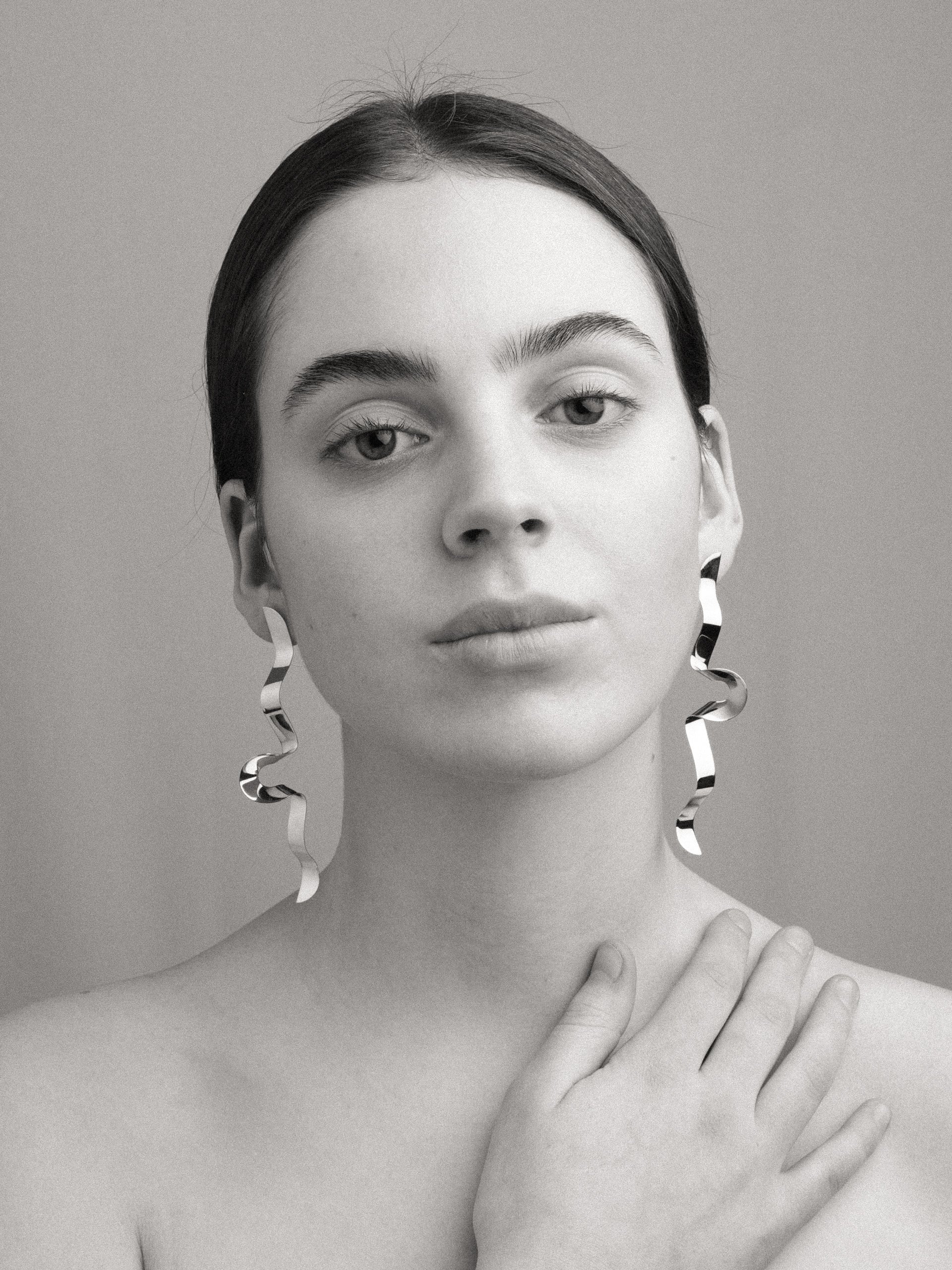 Black and white portrait of a person wearing large sculptural silver earrings with a neutral background