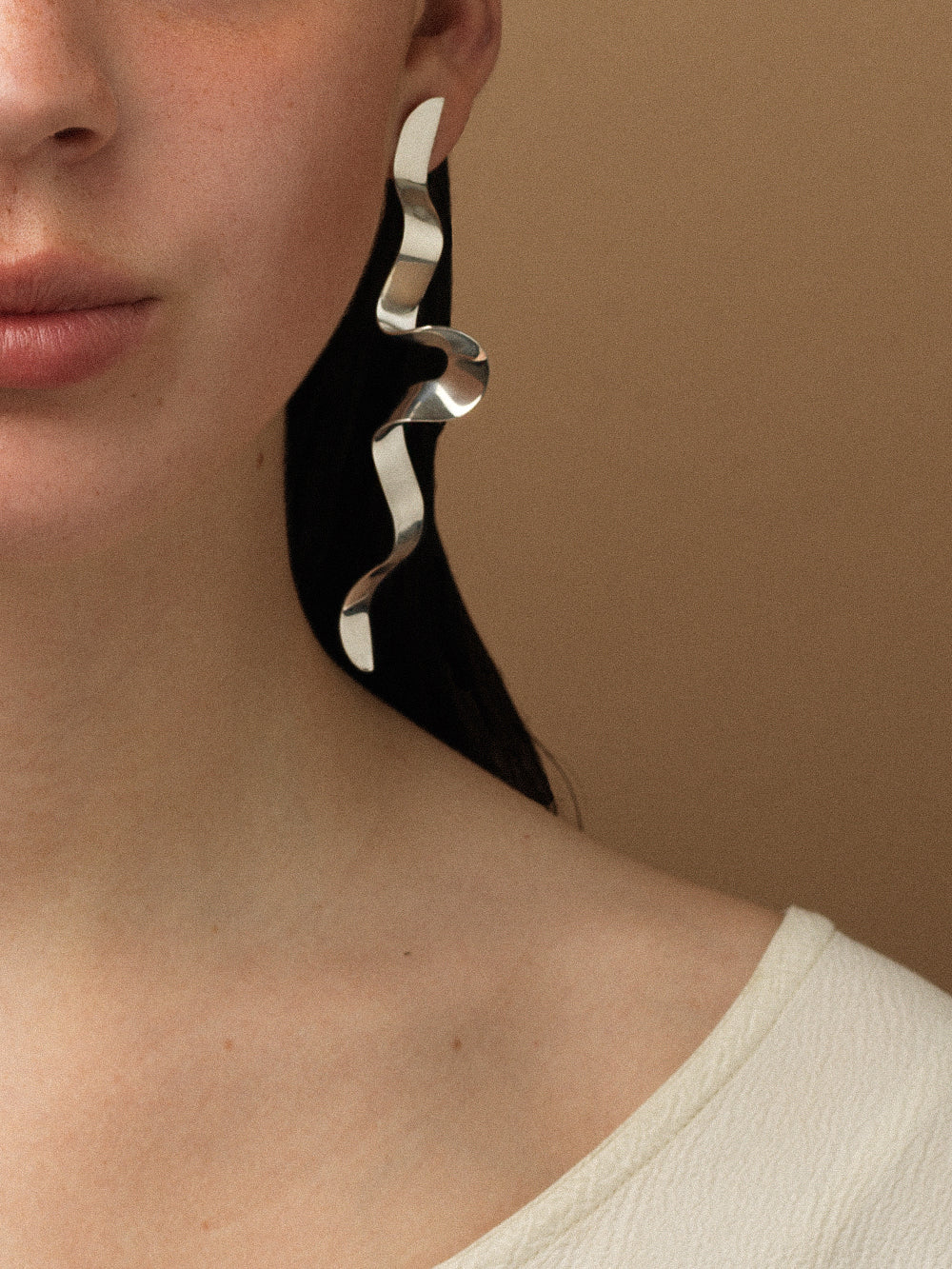 Close-up of a person wearing a sculptural silver earring against a beige background