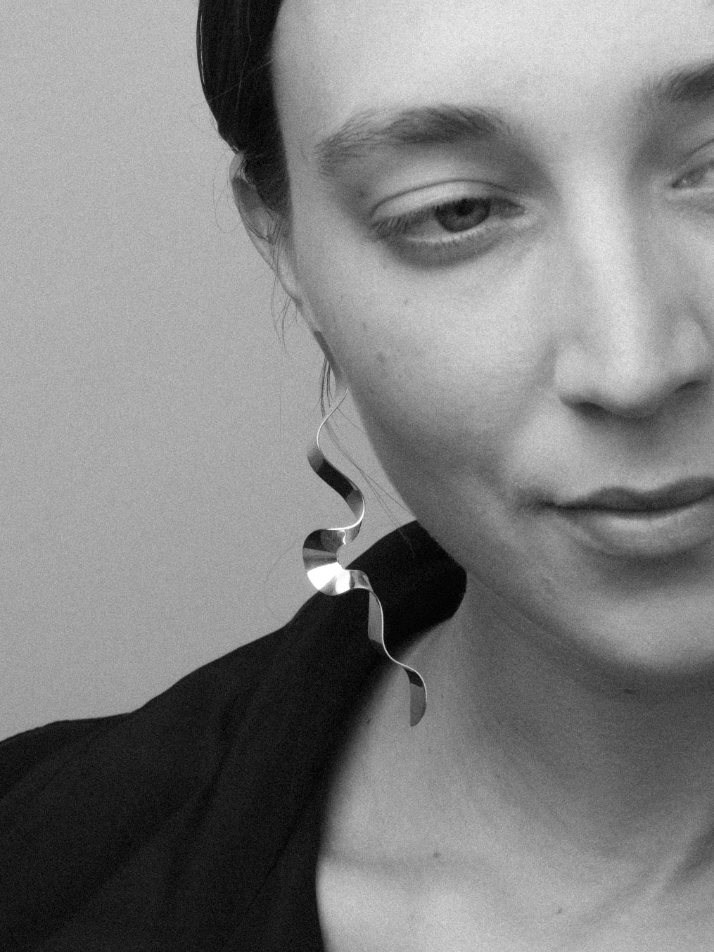Close-up of a person wearing a unique sculptural earring in silver against a neutral background